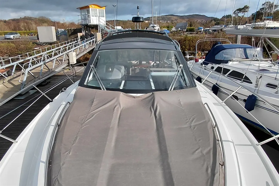 A view of a motorboat covered with a gray tarp, docked near a marina with other boats and a watchtower in the background.